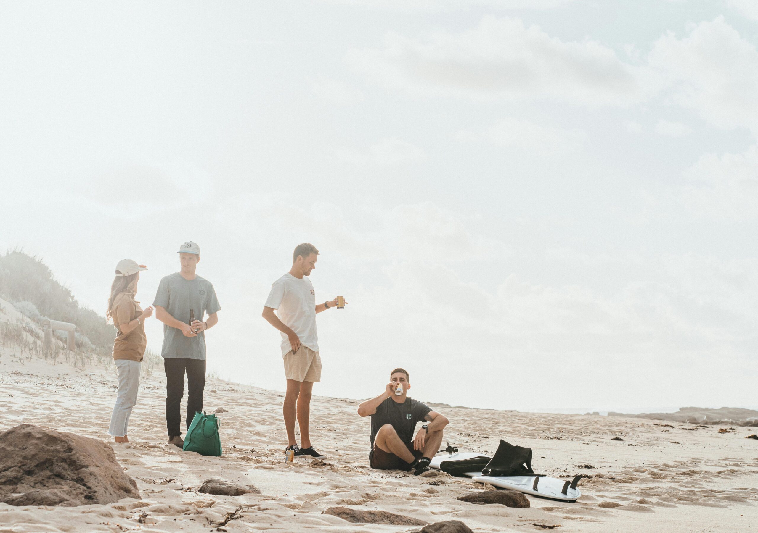 Group of friends relaxing on a beach, drinking and chatting in a sunny setting.